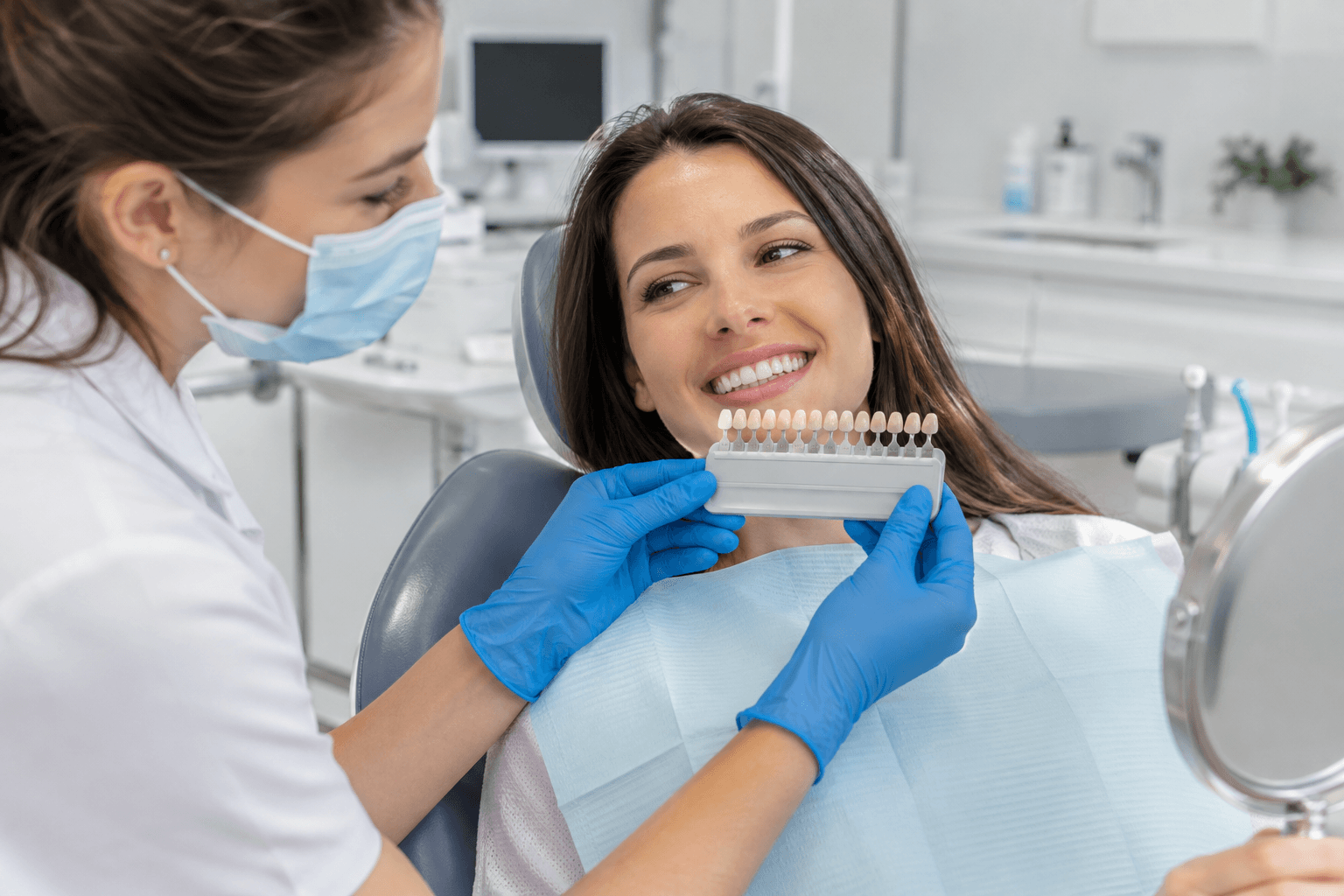 Dental professional holding a tooth shade guide beside a smiling patient